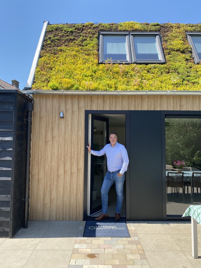 Een man in de open deur van een houten aanbouw met een groen sedumdak